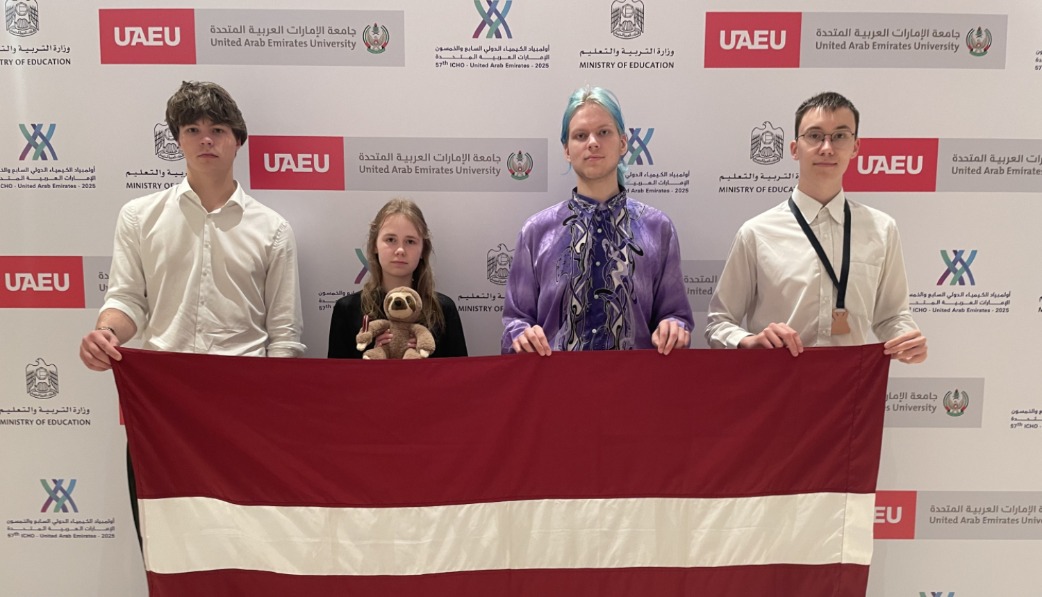 Latvijas komandas dalībnieki rokās ar LV karogu ķīmijas olimpiādē 2025 Dubaijā