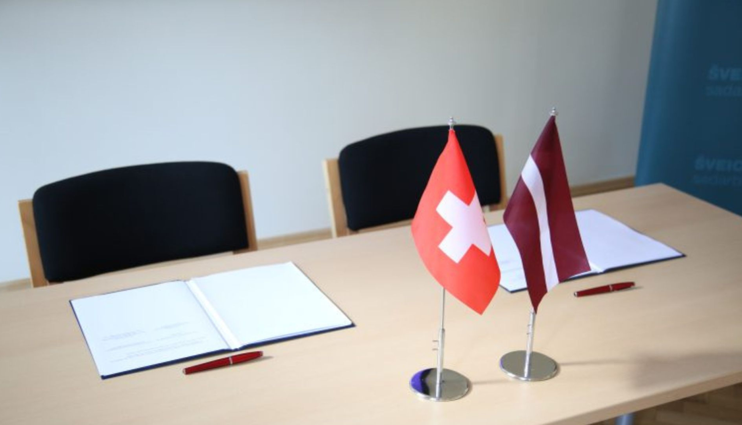 Galds ar atvērtu dokumentu un Latvijas, Šveices karogiem