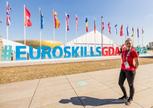 Meitene stāv fonā uzrakstam #EuroSkillsGdansk