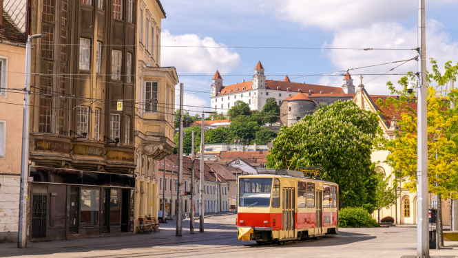 attēlā skats uz pili Bratislavā, priekšplānā brauc vecs tramvajs