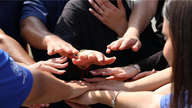 Erasmus vairāki cilvēki stāv aplī un saliek rokas kopā centrā