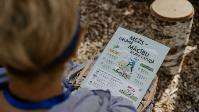 berns sez mežā ar plakātu rokās, uz kura rakstīts "Mežs - lielākā māčibu klase"