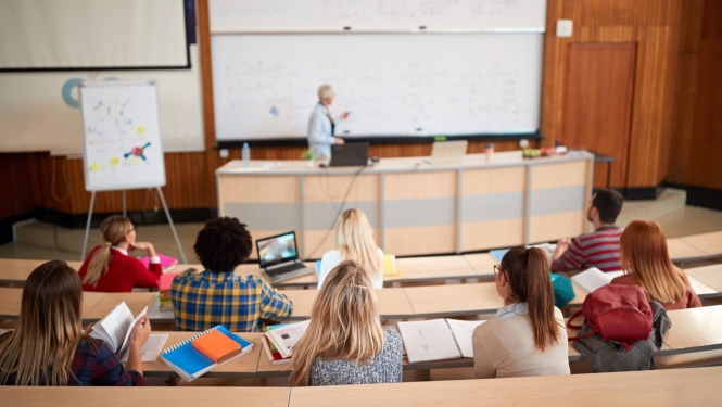 Augstskolas auditorijā lektors stāv pie lielas tāfeles, auditorijā sēž studenti un klausās