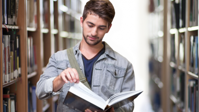 Vīrietis lasa grāmatu bibliotēkā