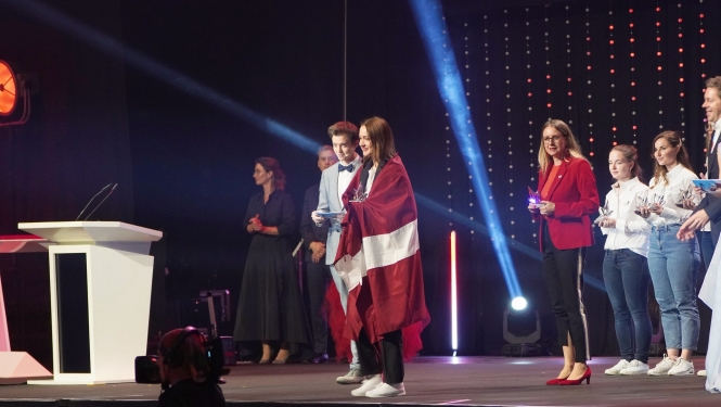 Meitene uz skatuves ar Latvijas karogu ap pleciem