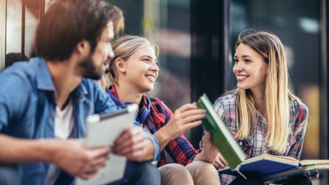 trīs studenti sēž uz trepēm ar grāmatām