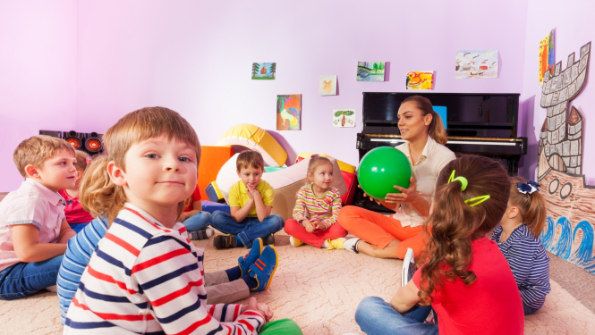 bērni sēž uz grīdas aplītīt kopā ar audzinātāju un spēlē attīstošās spēles