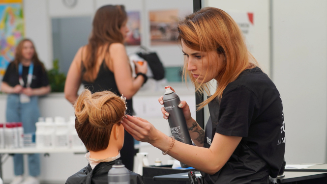 Friziere ar matu laku rokās veido matus manekena galvai