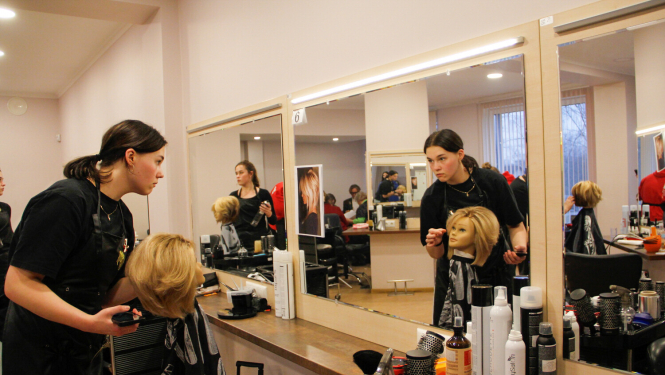 Meitene veido frizūru manekenam un skatās spogulī