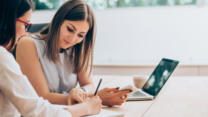 sieviete karjeras konsultante pieraksta kaut ko, blakus sēž jauna sieviete, blakus uz galda stāv portatīvais dators