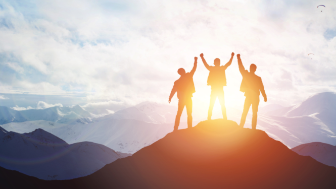 Cilvēki stāv kalna galā ar rokām gaisā