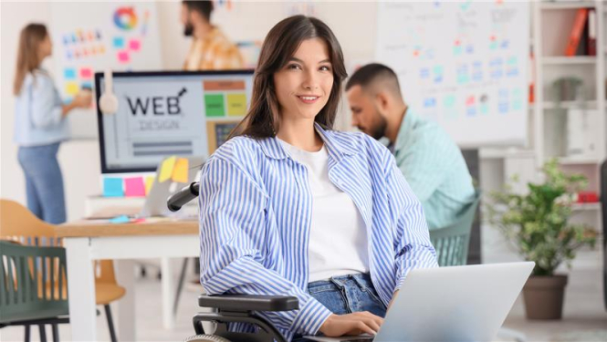 jauna meitene sēž krēslā klēpī tur portatīvo datoru, aizmugurē kāds strādā