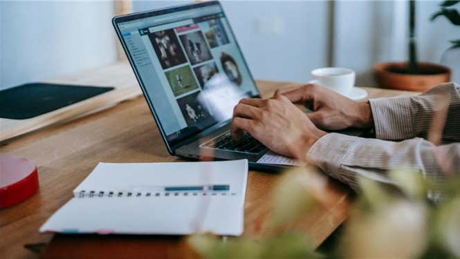 cilvēks strādā pie galda ar portatīvo datoru, blakus uz galda ir pierakstu klade