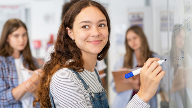 Jauniete raksta uz tāfeles ar flomasteru