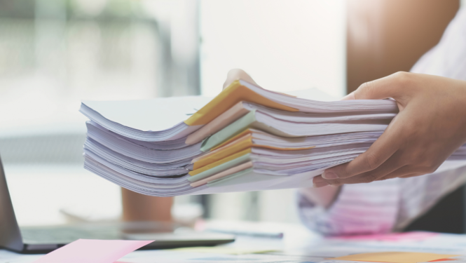 sieviete tur rokās kaudzi ar drukātiem dokumentiem virs galda