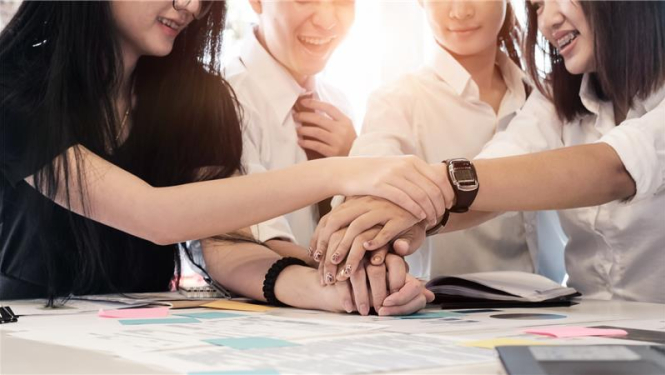 vairāki jaunieši salikuši rokas kopā vienu virs otras un smaida