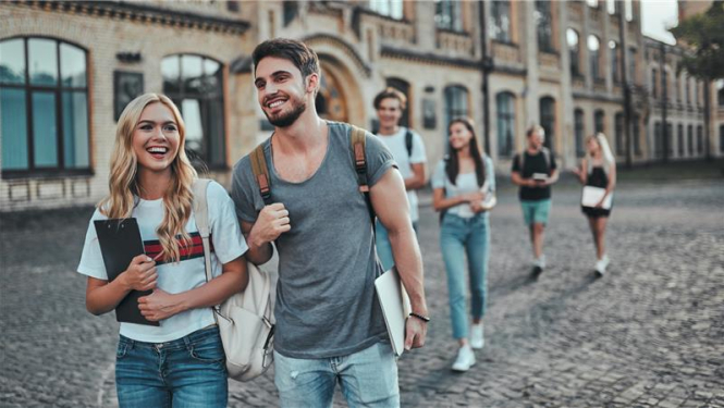 divi studenti iet pa ceļu blakus universitātei, rokās mapes