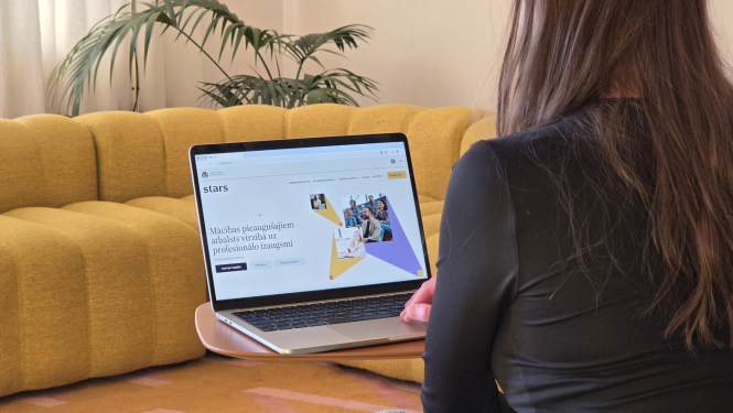 Esi Starā, sieviete sēž ar muguru, klēpi viņai atvērts dators, kur uz ekrāna ir redzama www.stars.gov.lv mājaslapa