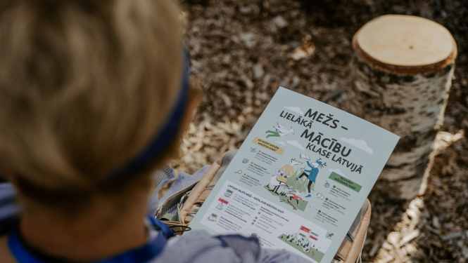 berns sez mežā ar plakātu rokās, uz kura rakstīts "Mežs - lielākā māčibu klase"