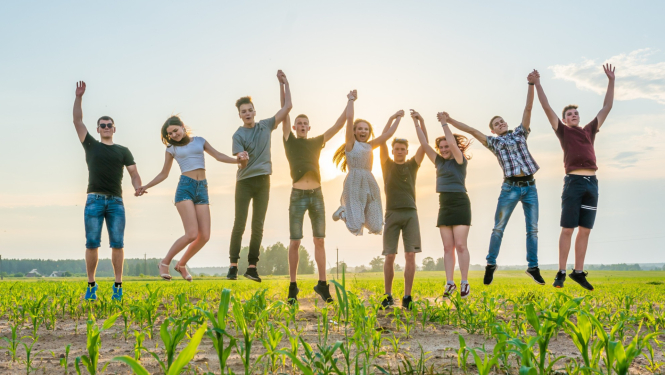 Vairāki studenti priecīgi sadevušies rokās palecas gaisā zaļā pļavā