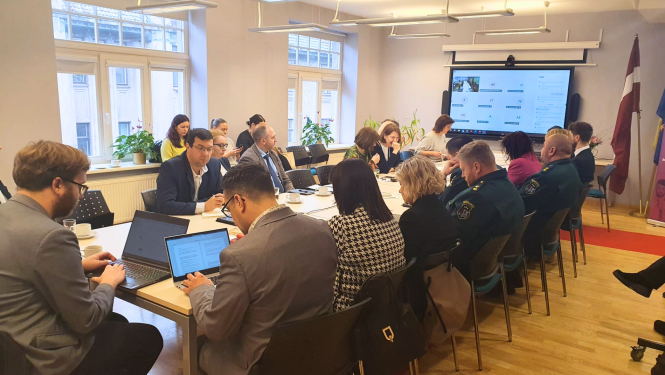 Cilvēki zālē sēž pie galdiem