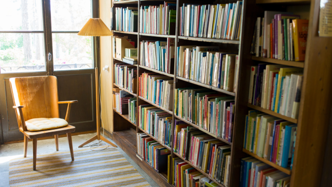 bibliotēkas gramatu plaukti blakus kresls ar stāvlampu lasīšanai