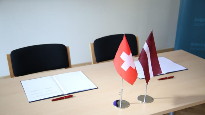 Galds ar atvērtu dokumentu un Latvijas, Šveices karogiem