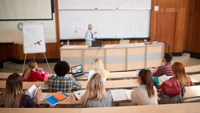 Augstskolas auditorijā lektors stāv pie lielas tāfeles, auditorijā sēž studenti un klausās