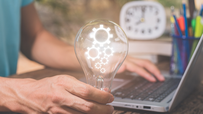 Vīrieša roka, atstutēta pret galdu, tur ieslēgtu spuldzi blakus datoram