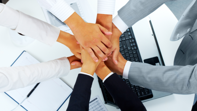 Cilvēki biznesa vidē salikuši rokas vienu otrai virsū