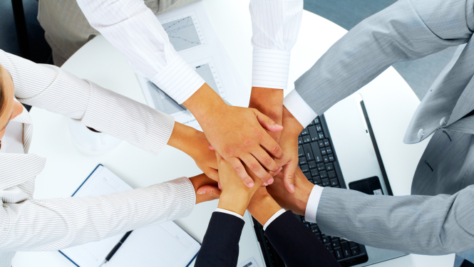 Seminārā virs galda dalībnieki ir salikuši rokas rokā, lai simbolizētu komandu