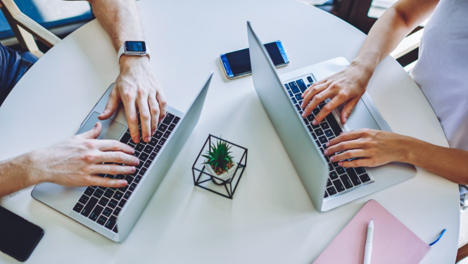 sieviete un vīrietis strādā pie portaīviem datoriem blakus uz galda ir pierakstu klade un telefons