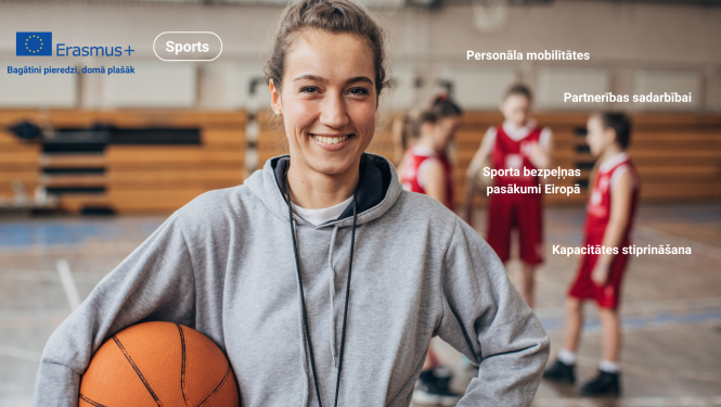 jauna trenere smaidiga stāv ar bumbu sporta zālē, aizmugurē stāv bērni