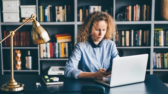 sieviete strādā pie portatīvā datora pie galda bibliotēkā