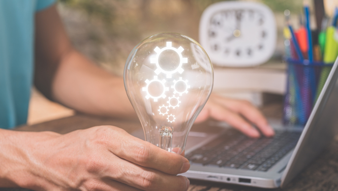 rokā tur lampiņu ar zobratiem pie portatīvā datora