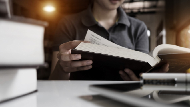 jauns virietis sez biliotekā pie galda ar grāmatu rokās 