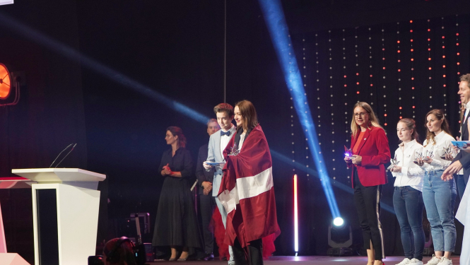 Meitene uz skatuves ar Latvijas karogu ap pleciem