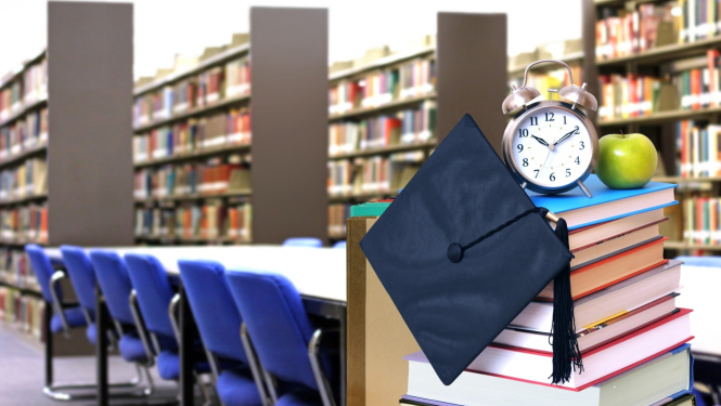 gramatu kaudzīte uz galda bibliotēkā virsū pulkstenis un ābols