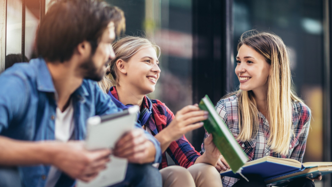 trīs studenti sēž uz trepēm ar grāmatām