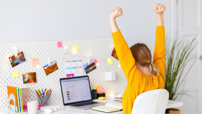 jauna sieviete priecīgi pacēlusi rokas uz augšu pie darba datora