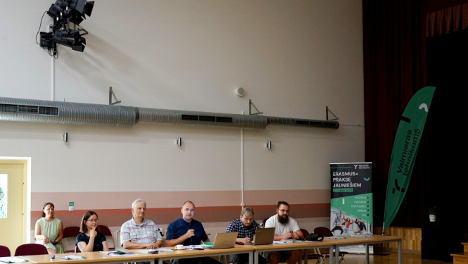 Cilvēku grupa sēž pie galva lielajā sporta hallē