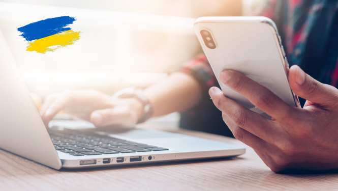 virietis strada pie datora un rokas tur telefonu. Attēlam ir uzlikts Ukrainas karogs