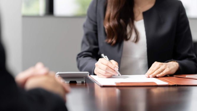 sieviete pieraksta uz papīra lapas piezīmes darba intervijā, pretī viņai sēž intervējamais