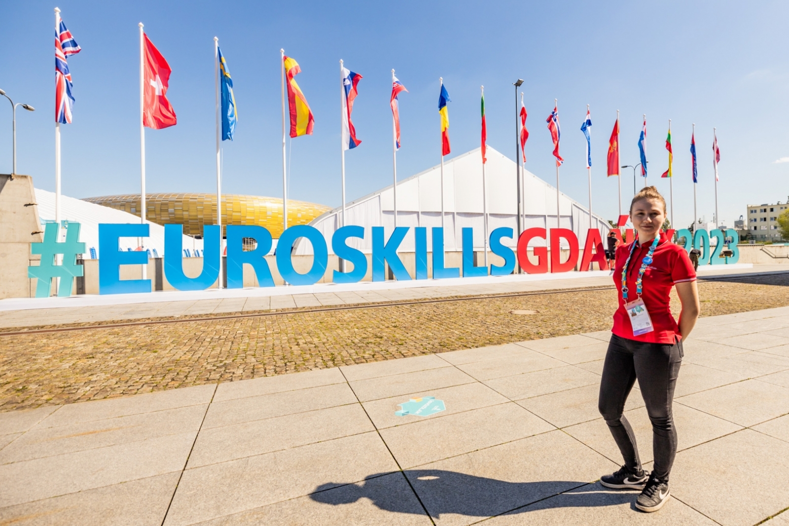 Meitene stāv fonā uzrakstam #EuroSkillsGdansk