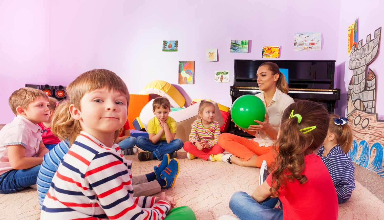 bērni sēž uz grīdas aplītīt kopā ar audzinātāju un spēlē attīstošās spēles