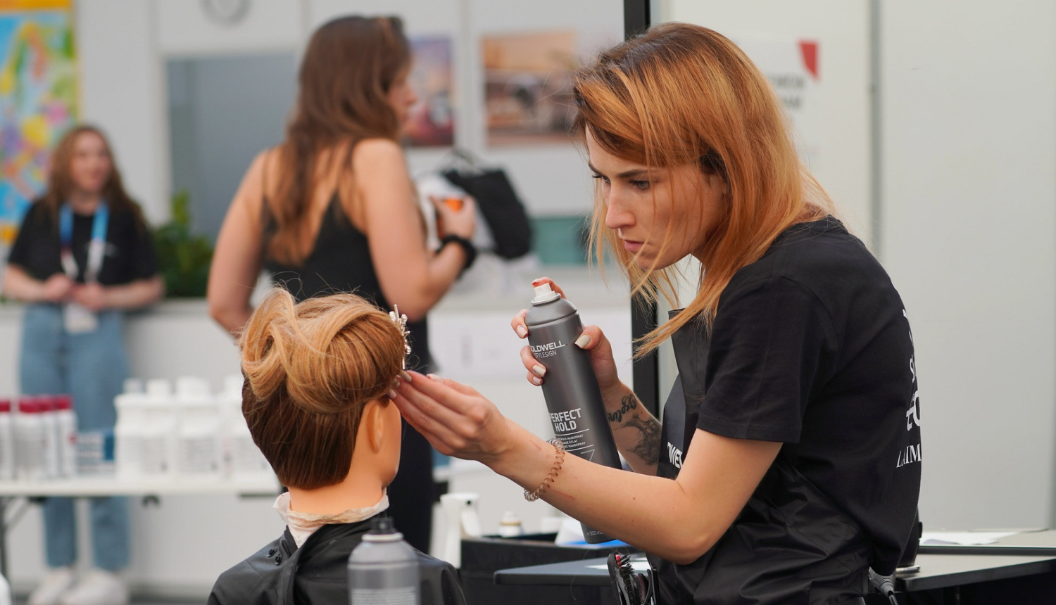 Friziere ar matu laku rokās veido matus manekena galvai