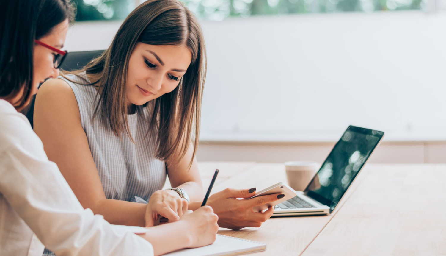 sieviete karjeras konsultante pieraksta kaut ko, blakus sēž jauna sieviete, blakus uz galda stāv portatīvais dators
