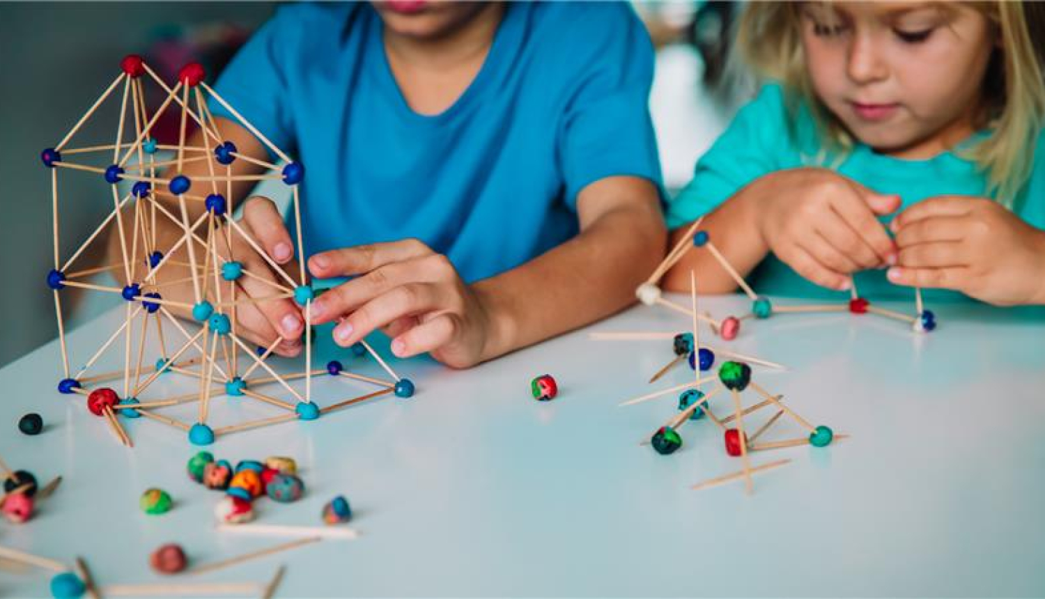 pirmskolas vecuma puika un meitene sēž pie galda un liek kopā konstruktoru