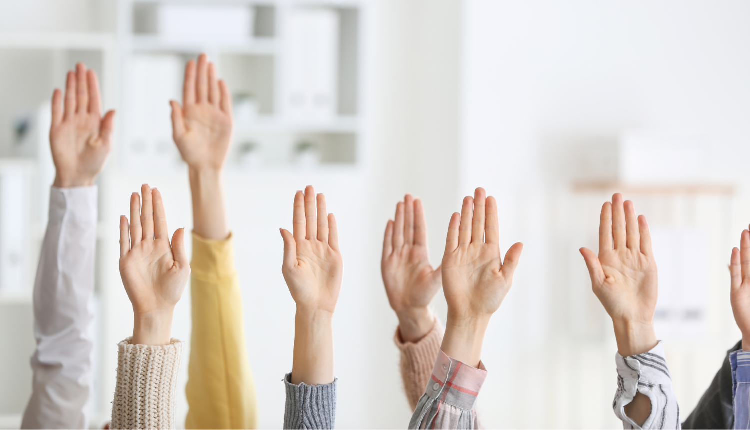 vairāku cilvēku rokas paceltas augšā, fonā biroja telpas