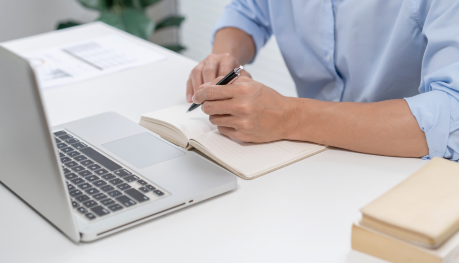 Cilvēks sēž pie galda ar portatīvo datoru un piezīmju bloknotu